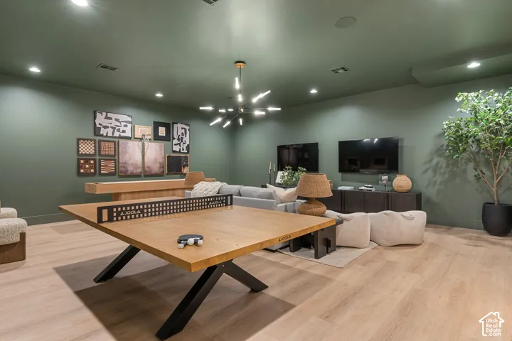 Spacious recreational room with light wood-finish flooring, recessed lighting, and a modern chandelier