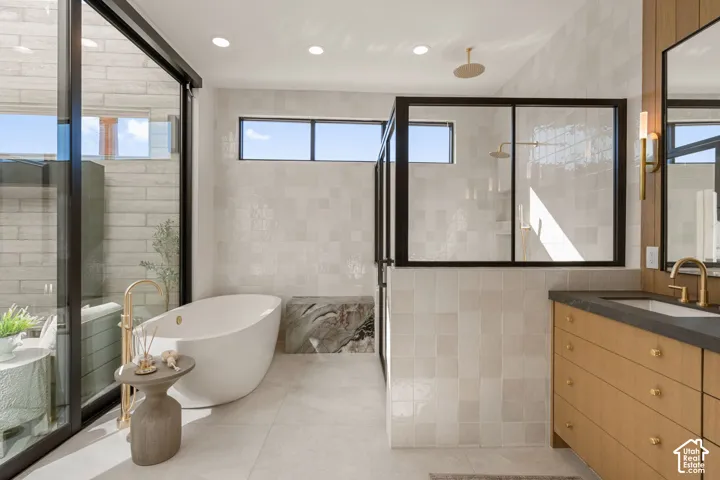 Freestanding soaking tub with gold-finish floor-mounted faucet, walk-in shower with black-framed glass enclosure, wood-finish vanity with dark countertop and undermount sink, and recessed lighting