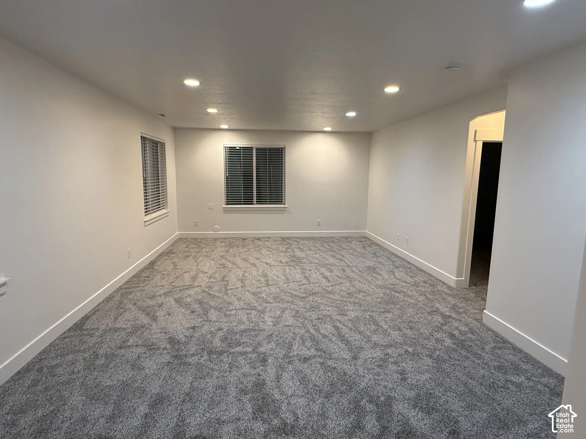 Expansive room with recessed lighting, two windows with blinds, and neutral-toned carpeting