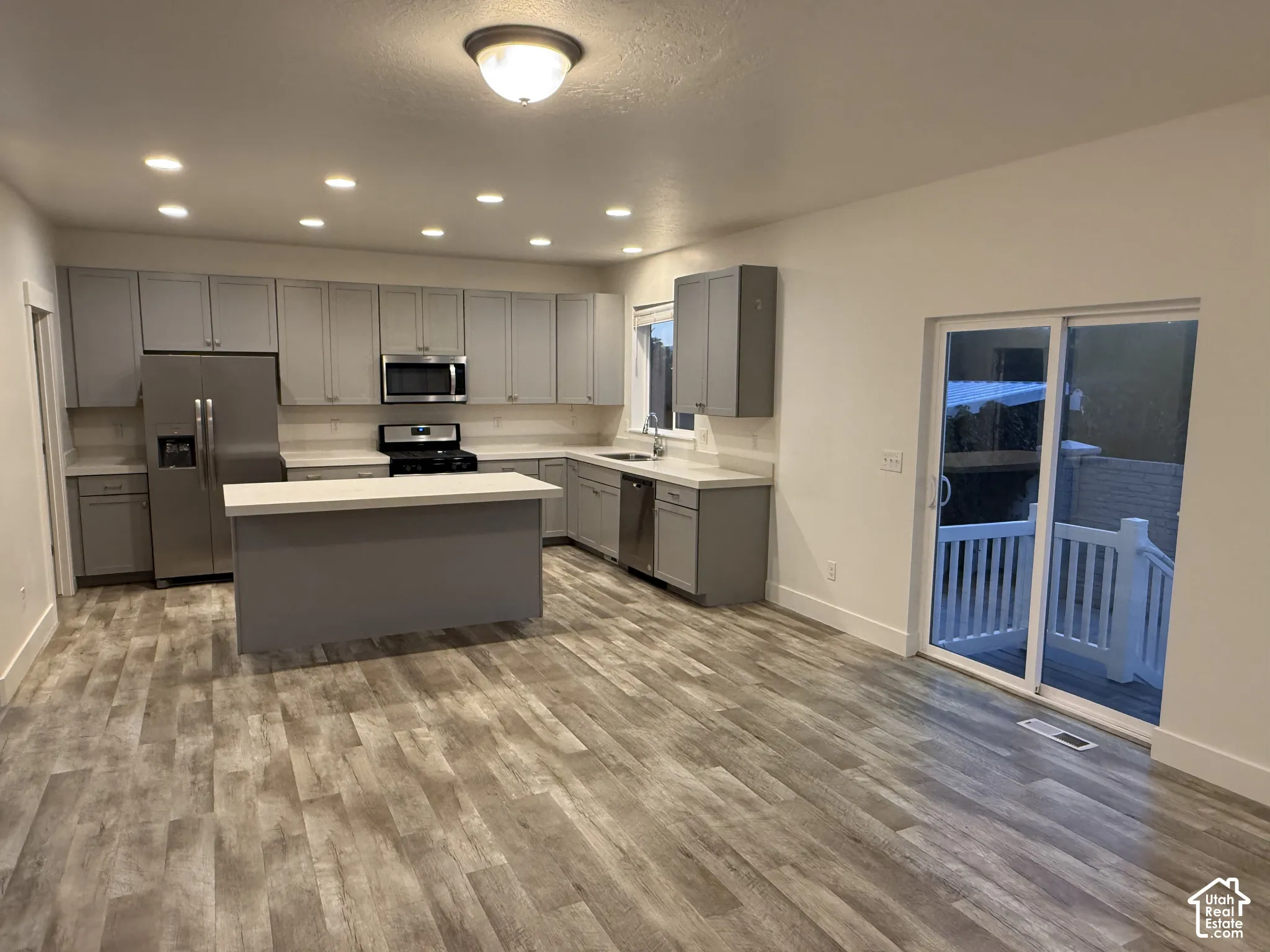 Kitchen featuring stainless steel appliances, light gray cabinetry, a central island with a light-toned countertop, and wood-finish flooring