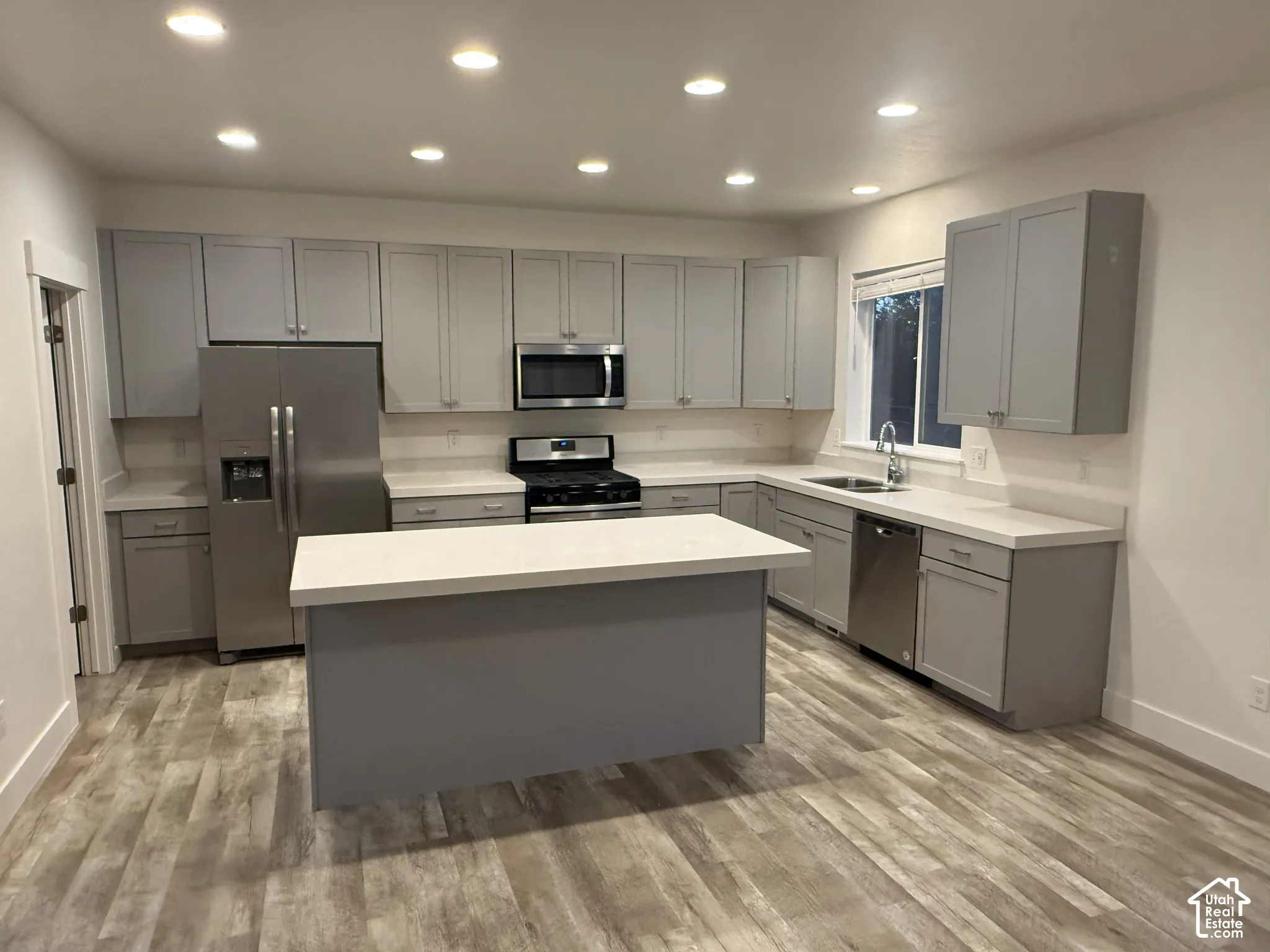 Kitchen with gray cabinetry, stainless steel appliances, white countertops, a central island, and wood-finish flooring
