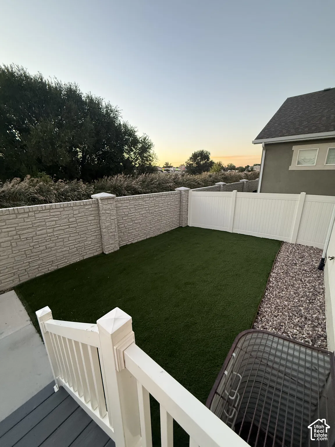 Enclosed backyard featuring artificial turf, a white vinyl fence, and a decorative stone-patterned privacy wall
