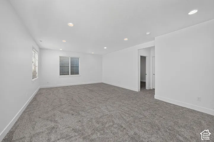 Spacious room with gray carpet, multiple windows with blinds, and recessed lighting