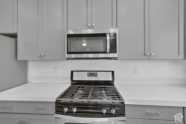 Gray shaker-style cabinetry with chrome hardware, white solid surface countertops, a stainless steel range, and an over-the-range microwave