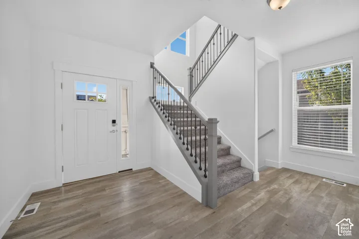 Entryway featuring wood-finish flooring, a white paneled door with glass inserts, a carpeted staircase with an iron baluster railing, and a window with blinds