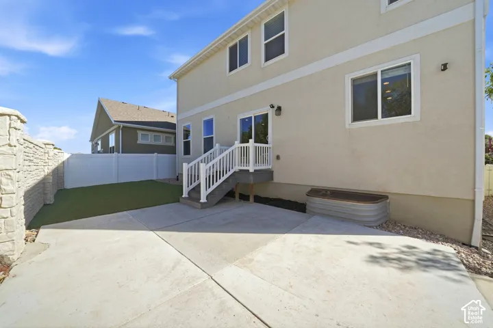 Exterior stucco siding, white vinyl fencing, concrete patio, artificial turf area, and a stone-clad retaining wall