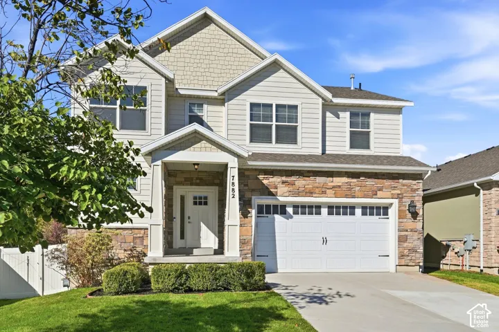 Two-story residence featuring a stone and siding exterior, an attached two-car garage, covered entry porch, and a manicured lawn