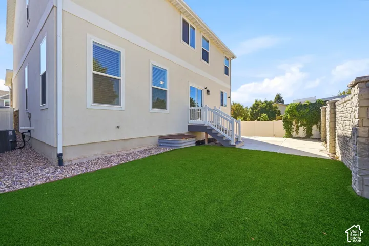 Rear exterior with a stone-finish privacy wall, artificial turf lawn, and a light-colored stucco finish