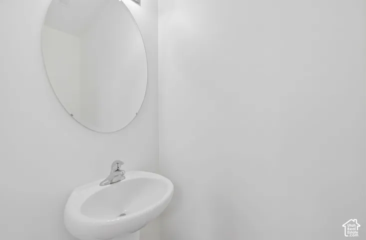 Pedestal sink with a chrome faucet, illuminated by an overhead light, complemented by a large oval mirror