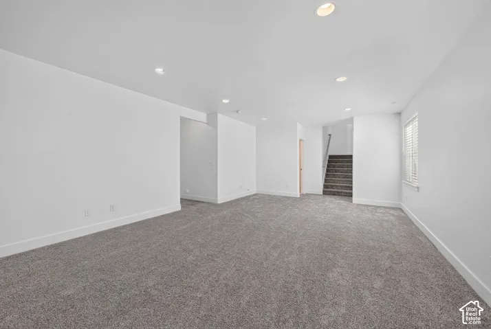 Recessed lighting, light gray carpeting, white walls, white window blinds, and a staircase with gray carpeted treads