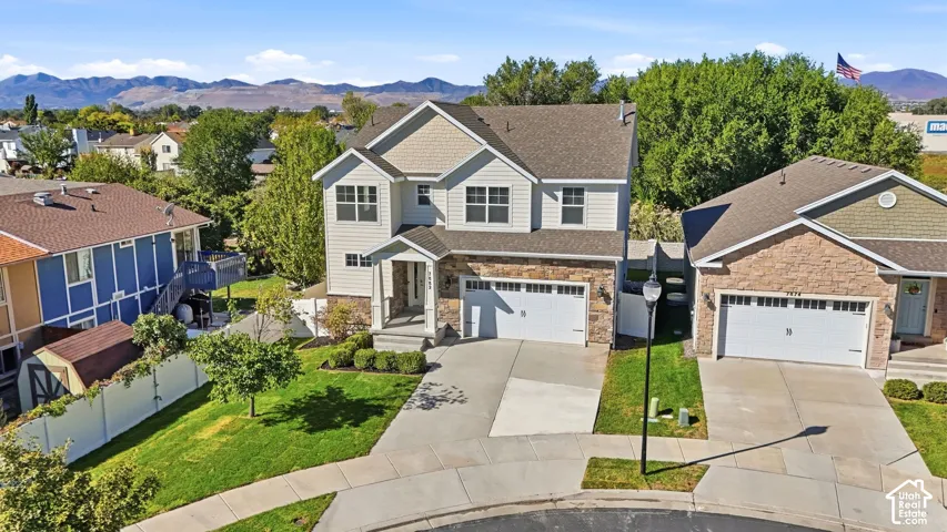 Two-story siding and stone exterior, attached two-car garage, concrete driveway, and front lawn