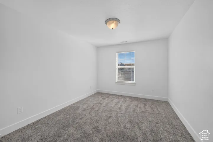 Neutral white wall color, single window with blinds, ceiling-mounted light fixture, and grey carpet flooring