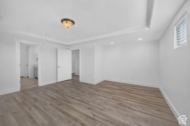 Wood-finish flooring, recessed lighting, white walls, and a tray ceiling