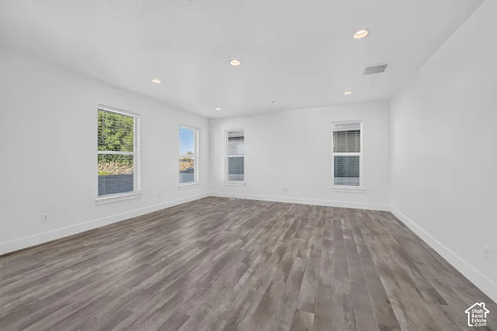 Spacious room featuring wood-finish flooring, white walls, multiple windows, and recessed ceiling lighting