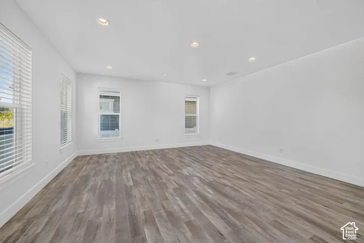 Recessed lighting and multiple windows illuminate this room featuring wood-finish flooring and neutral wall tones