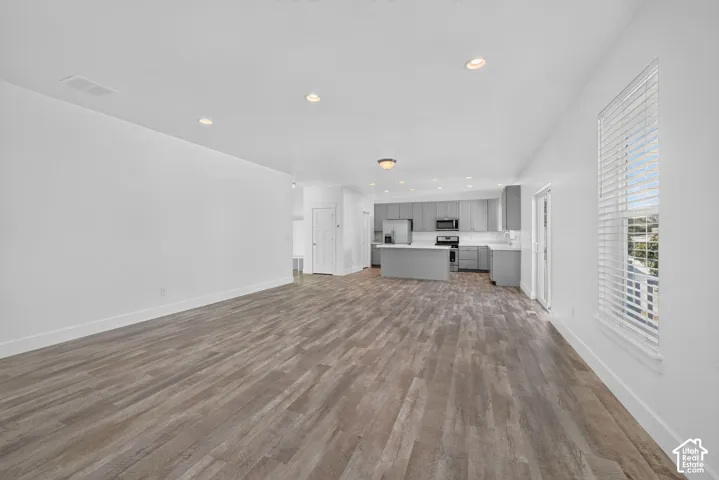 Open-concept living space featuring wood-finish flooring, recessed lighting, and a kitchen with grey cabinetry, a center island, and stainless steel appliances