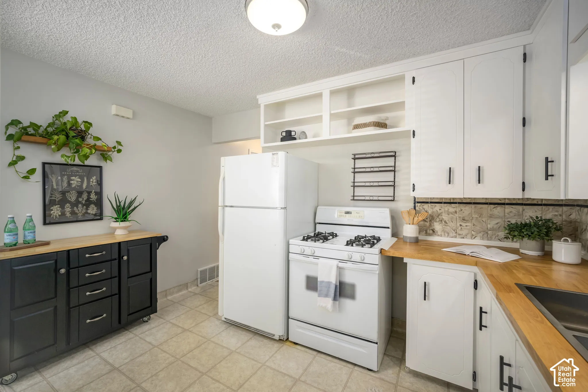 Functional kitchen featuring white cabinetry, light wood-finish countertops, tile flooring, and a gas range