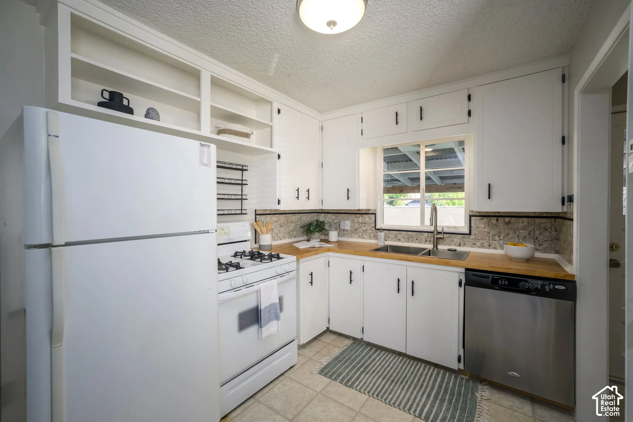 Kitchen featuring white cabinetry, light-toned countertops, a mosaic tile backsplash, and a stainless steel dishwasher