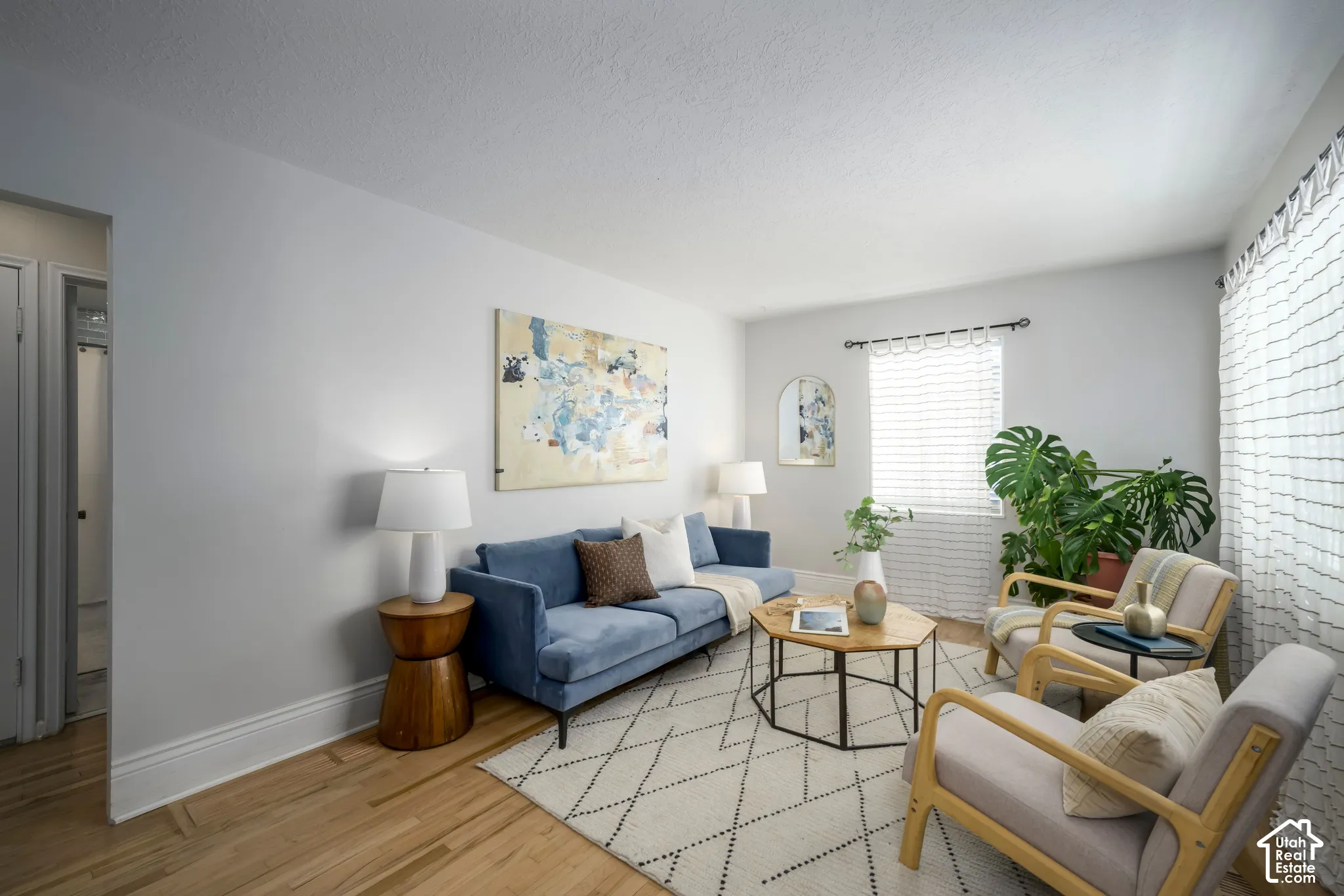 Light wood-finish flooring with white baseboards, bright white walls, and a window with blinds