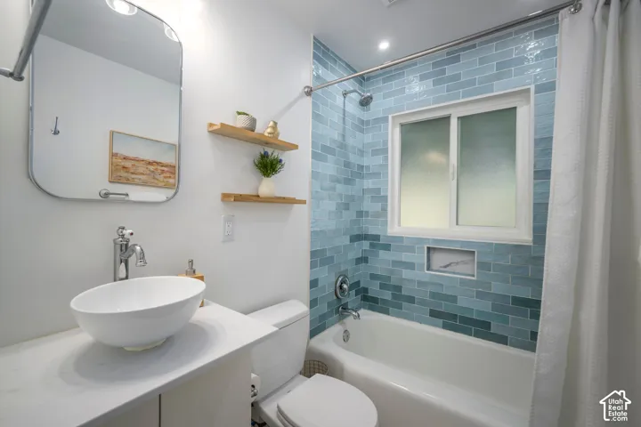 Bathroom featuring a vessel sink, integrated vanity, and a shower-tub combination with blue subway tile