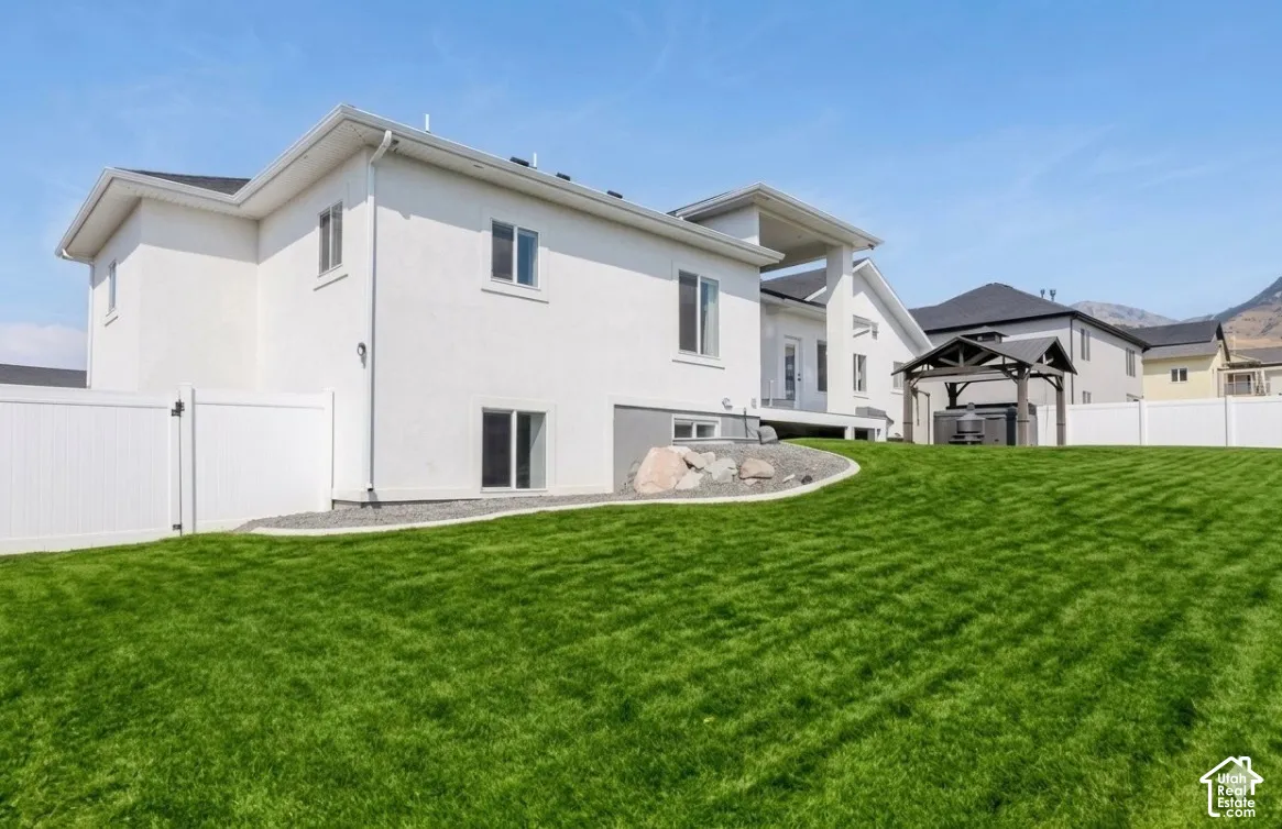Expansive green lawn with a white vinyl fence, gravel landscaping, and a covered gazebo