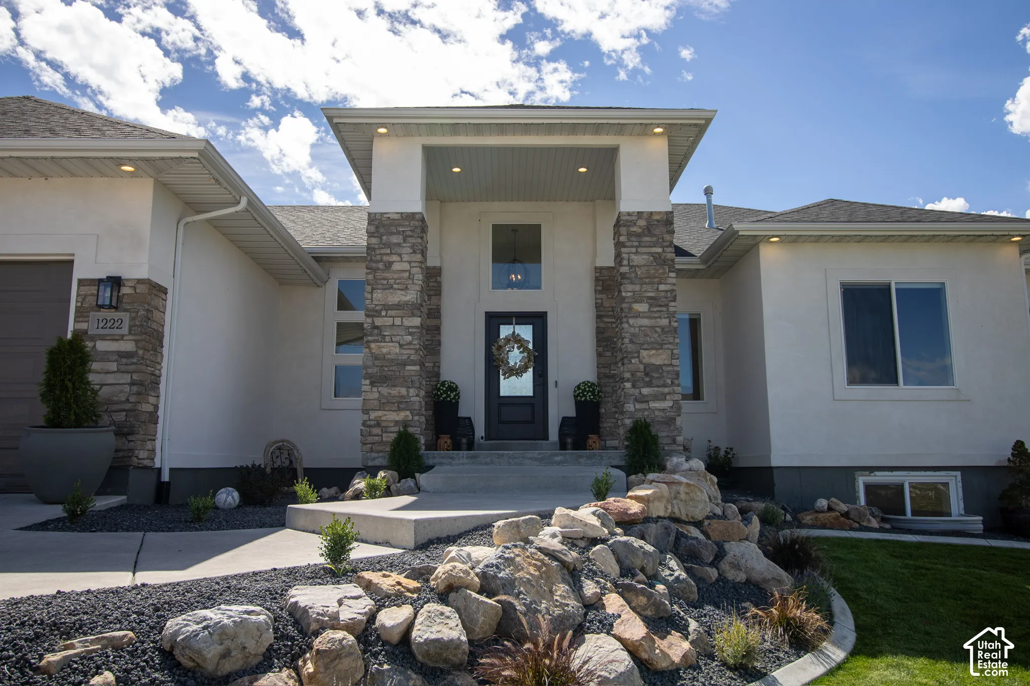 Stucco exterior with stone accents, covered entry, integrated garage, and a rock garden