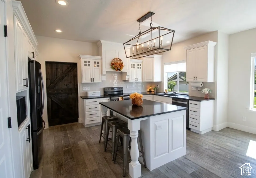 Kitchen featuring white cabinetry, wood-finish flooring, a central island with countertop, a tile backsplash, and a dark-finish barn door