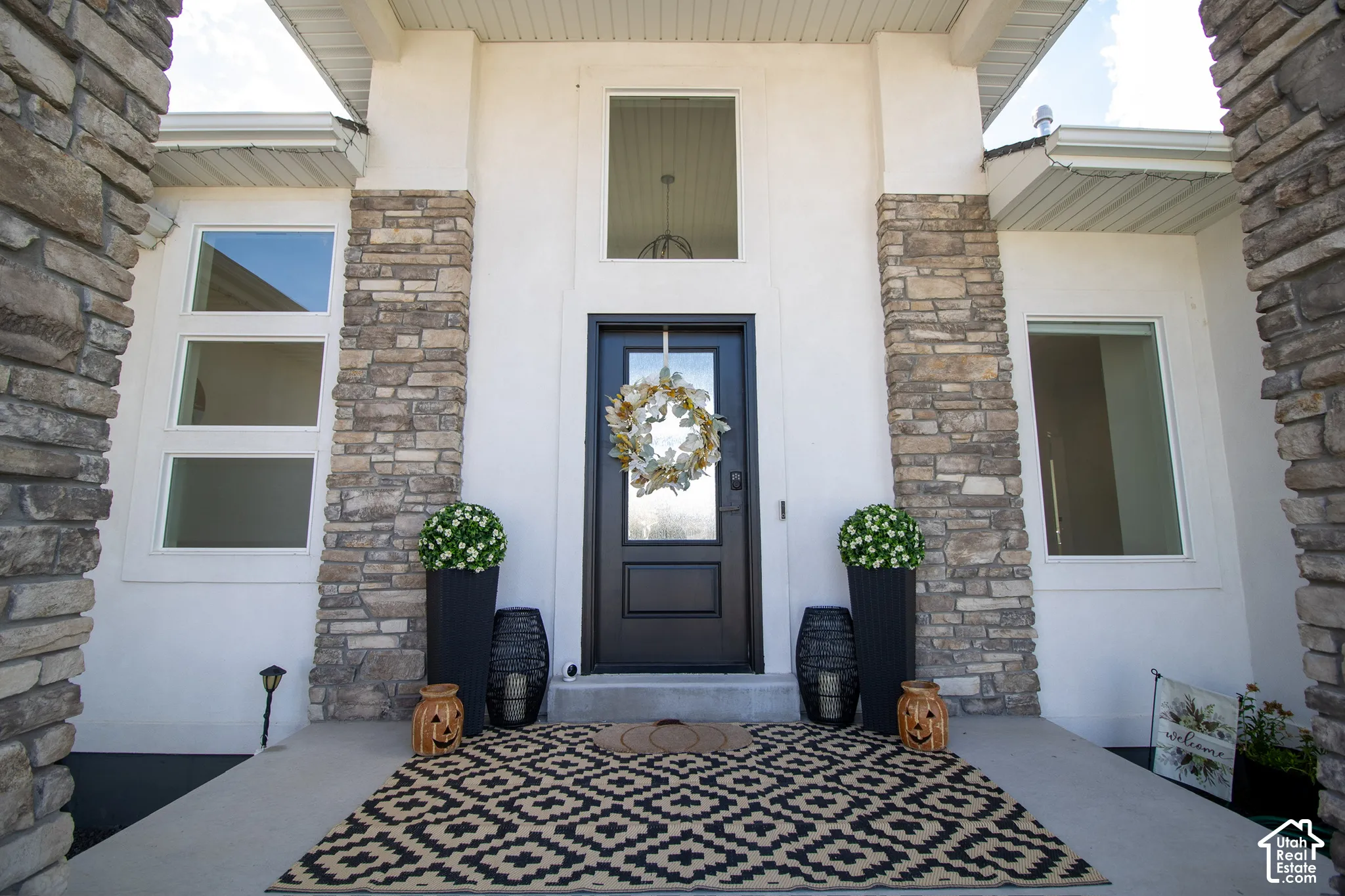 Welcoming front entry featuring a navy blue door with decorative wreath, flanked by stacked stone pillars and white fiber cement siding