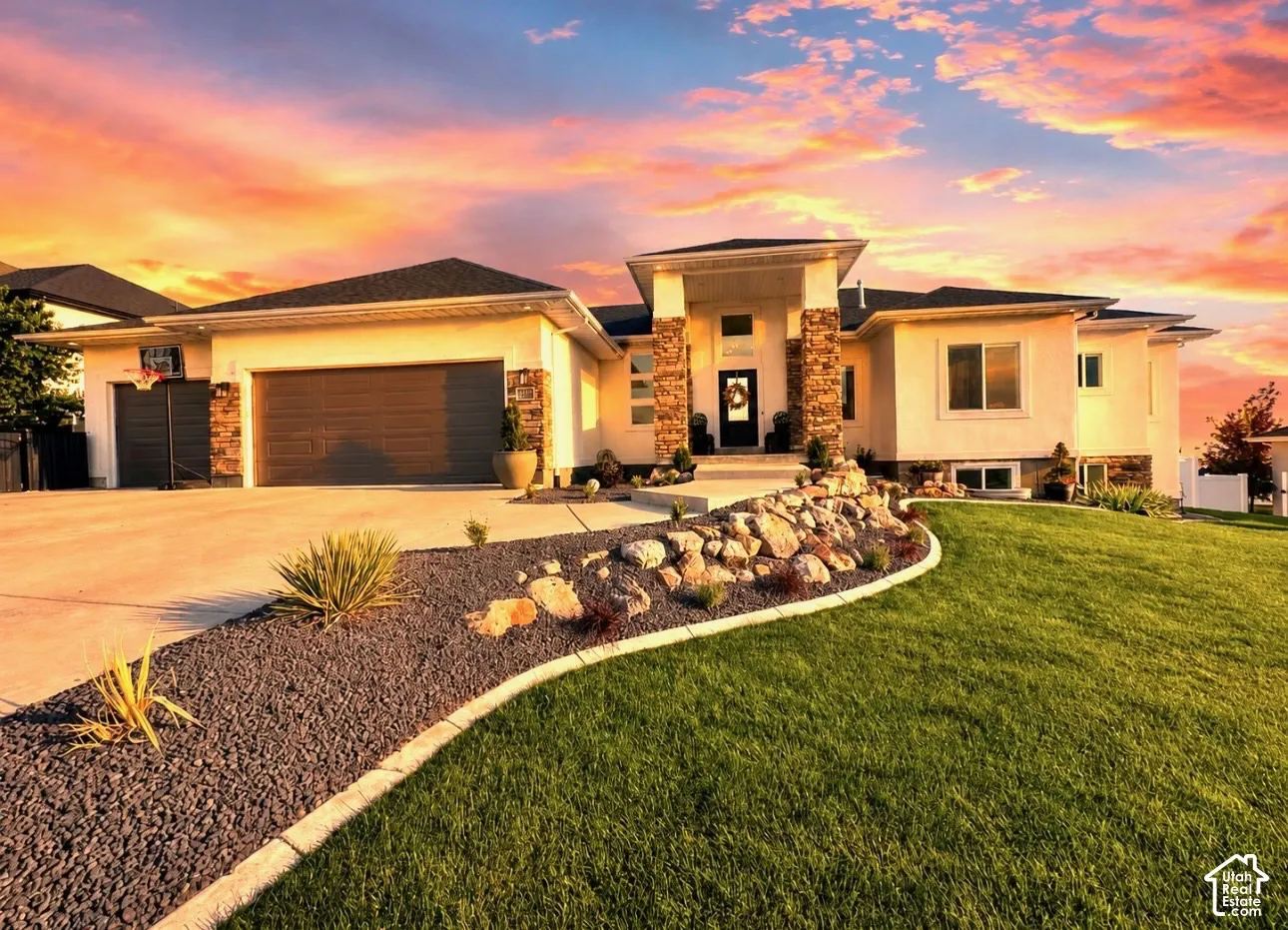 Exterior featuring stucco siding, stone column accents, a two-car garage, a concrete driveway, and a landscaped front yard with a rock garden