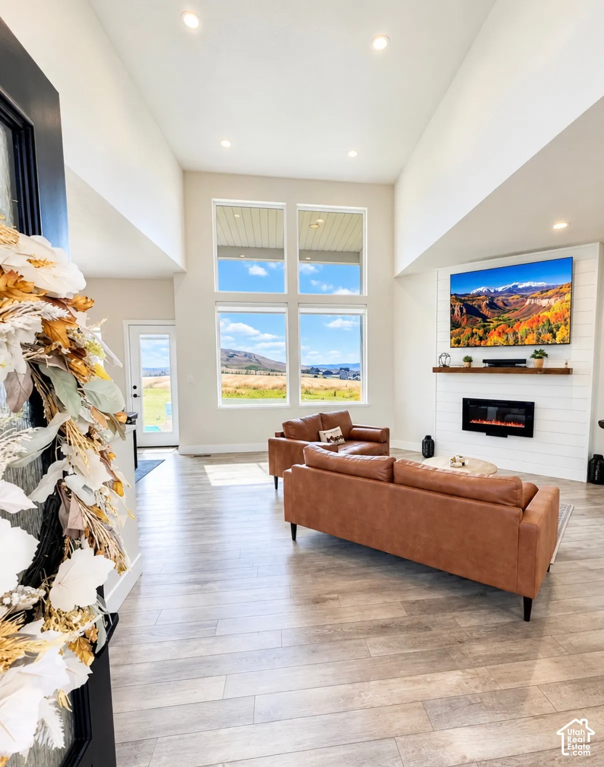 Vaulted ceilings with recessed lighting, large multi-pane windows, wood-finish flooring, and a fireplace with a wood mantle and shiplap-style surround
