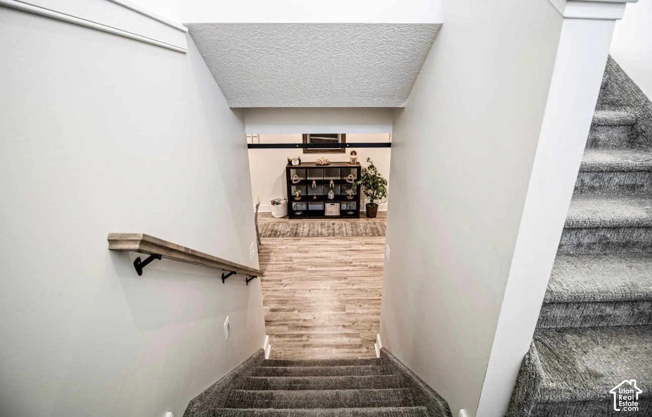 Carpeted staircase with a wood-finish handrail leading to a lower level featuring wood-finish flooring and a barn door