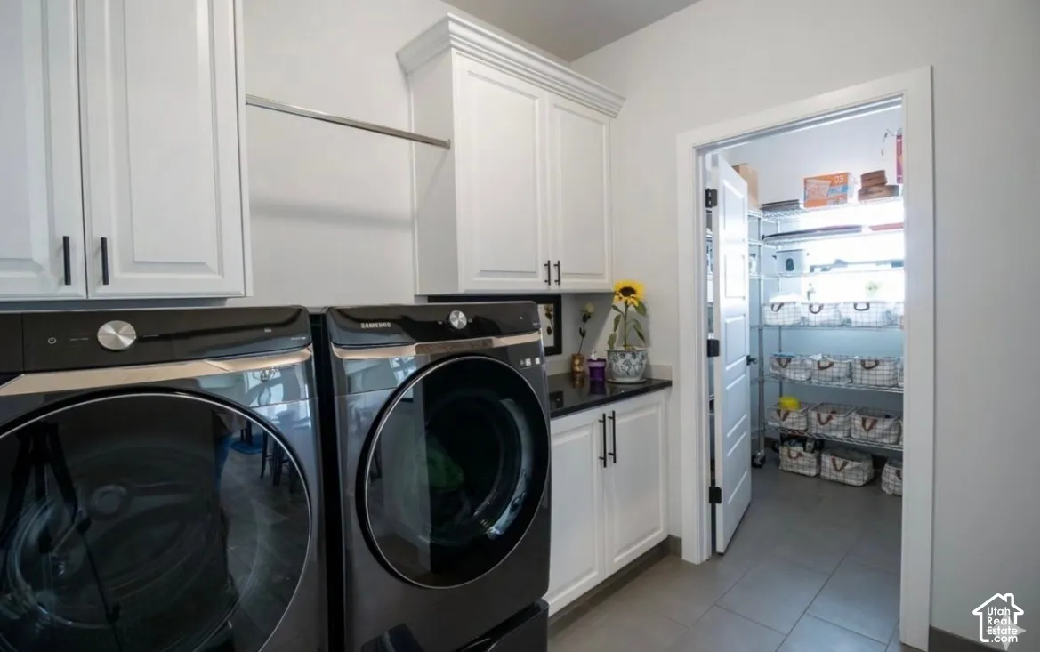 Laundry area with white cabinetry, a black countertop, and tile flooring