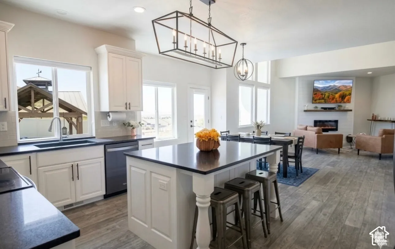 Open concept living space featuring wood-finish flooring, white cabinetry, a kitchen island with seating, pendant lighting, and a fireplace with a mantel
