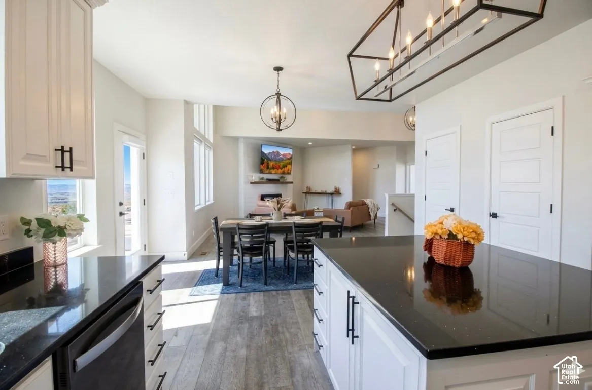 White shaker-style cabinetry with black hardware, dark countertops, wood-finish flooring, and a contemporary dining chandelier