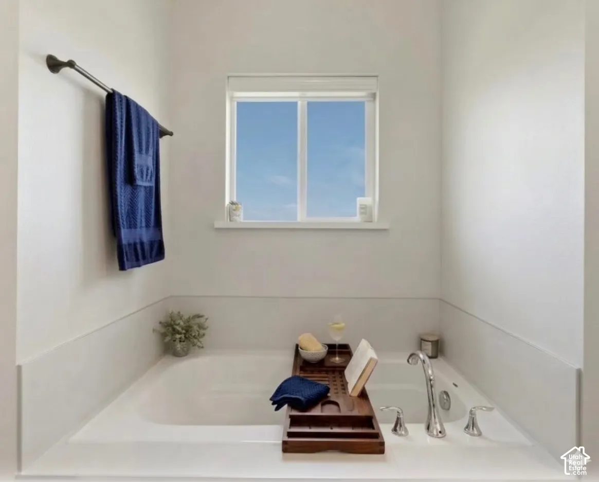 Built-in soaking tub with deck-mounted chrome fixtures, a window above, and a dark bronze towel bar
