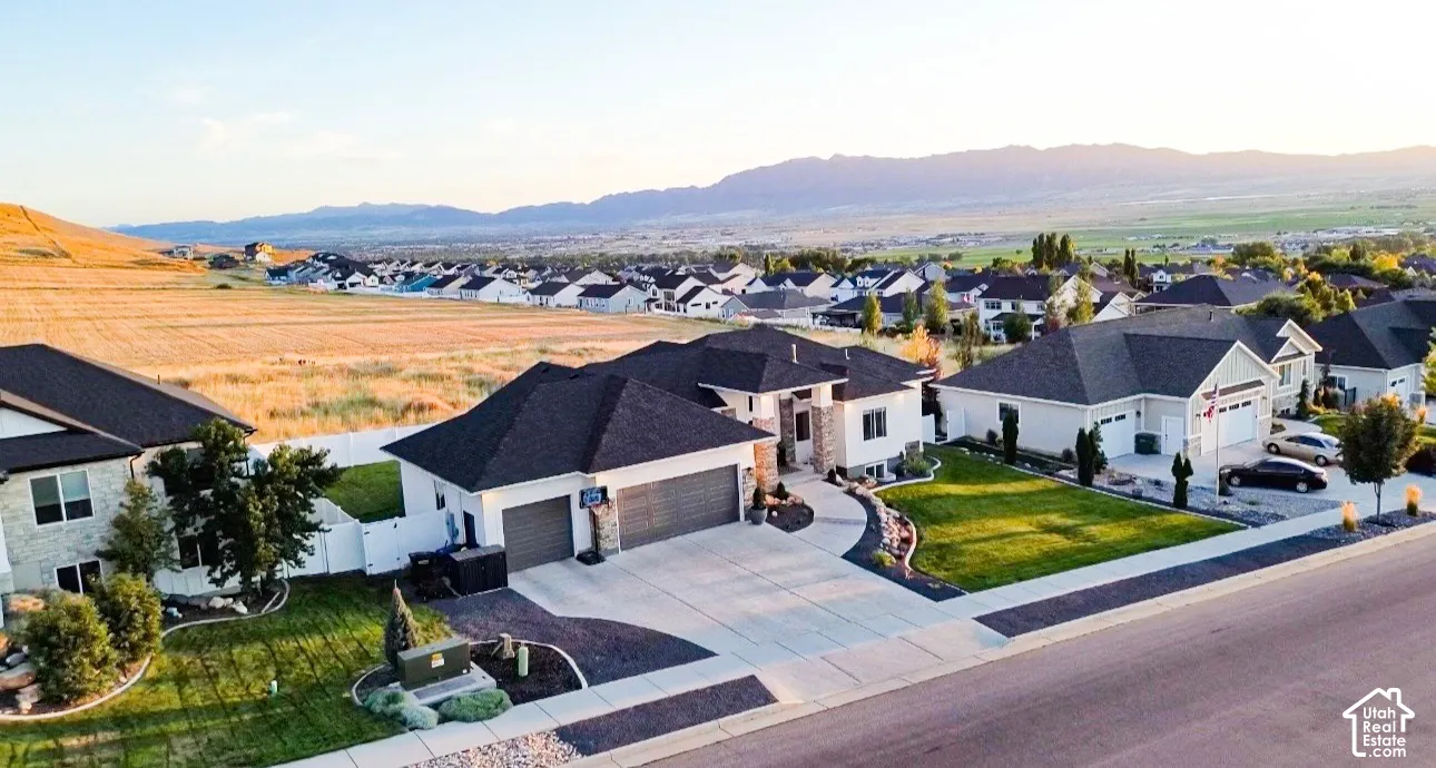 Expansive neighborhood with distant mountainous terrain, showcasing a concrete driveway, attached garage, and manicured landscaping