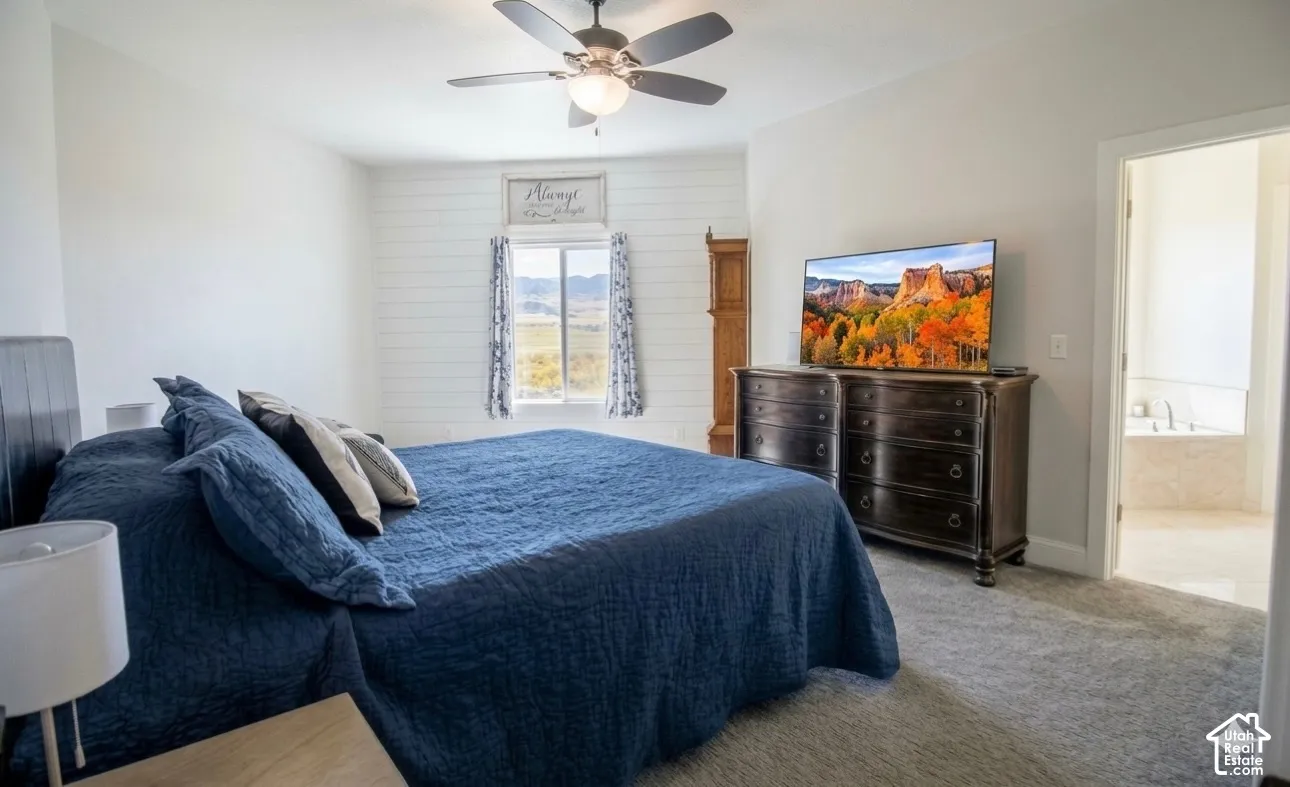 Carpeted bedroom featuring a ceiling fan, shiplap accent wall, and an open doorway revealing a jetted tub
