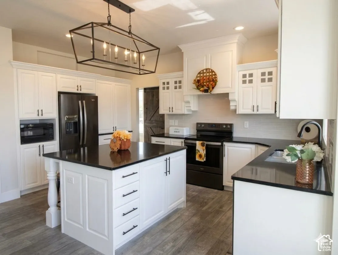 Kitchen featuring white cabinetry, dark countertops, wood-finish flooring, a center island with storage, and a black appliance package