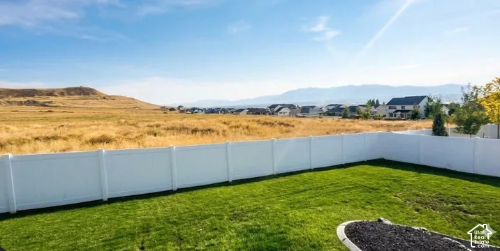 Expansive backyard featuring a manicured lawn, white privacy fencing, and a landscaping bed with dark ground cover