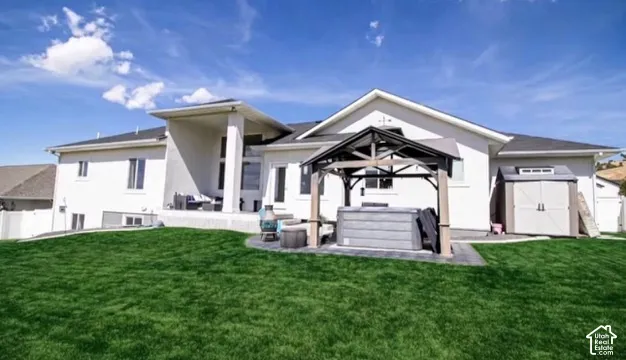 Expansive lawn with a white stucco exterior, covered patio, dark asphalt shingle roof, and a built-in outdoor storage shed