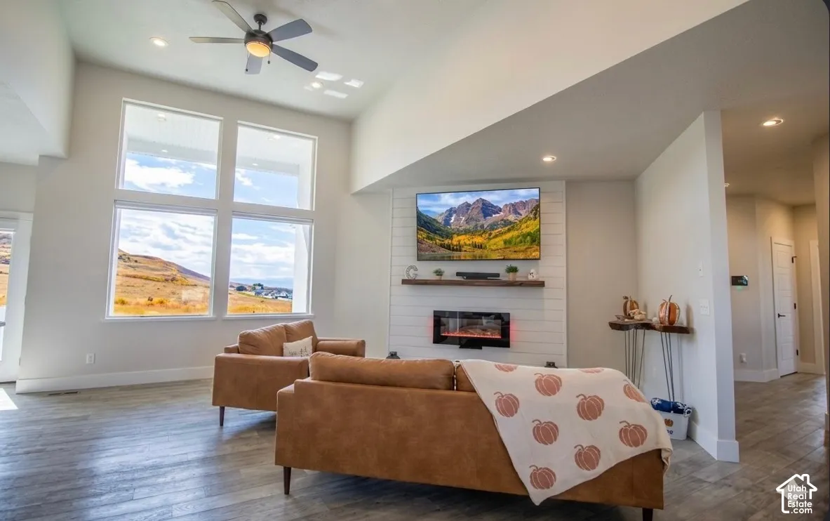 Vaulted ceilings, large multi-pane windows, wood-finish flooring, a contemporary fireplace, and a ceiling fan