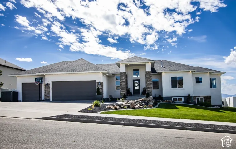Stucco exterior with stone accents, a multi-car driveway, attached garage, and a manicured front lawn