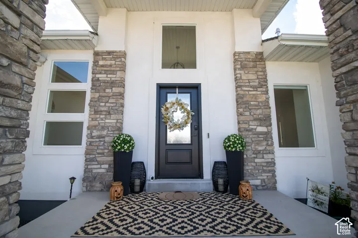 Welcoming front entry featuring a navy black door with decorative wreath, flanked by stacked stone pillars and white fiber cement siding
