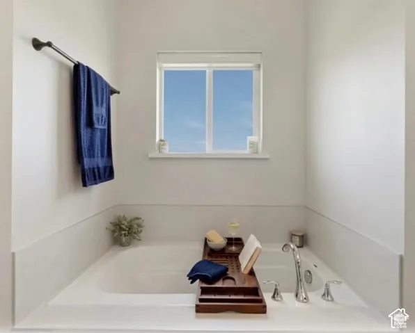 Built-in soaking tub with deck-mounted chrome fixtures, a window above, and a dark bronze towel bar