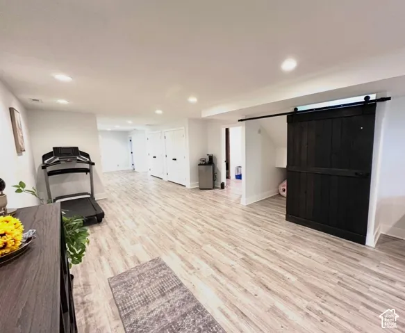 Spacious room featuring wood-finish flooring, recessed lighting, and a dark wood barn door on a black track