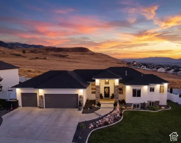 Modern architecture with a dark shingle roof, stone accent columns, a two-car garage, and established landscaping