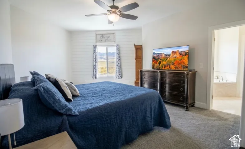 Carpeted bedroom featuring a ceiling fan, shiplap accent wall, and an open doorway revealing a jetted tub