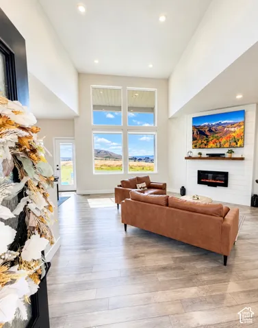 Vaulted ceilings with recessed lighting, large multi-pane windows, wood-finish flooring, and a fireplace with a wood mantle and shiplap-style surround