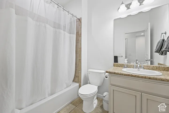 White bathtub with subway tile surround, tile flooring, vanity with light-toned countertop, integrated sink, and white cabinetry