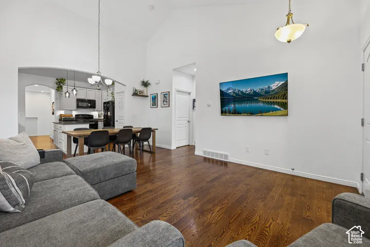 Vaulted ceilings, wood-finish flooring, kitchen island with seating, dark shaker cabinetry, and pendant lighting fixtures